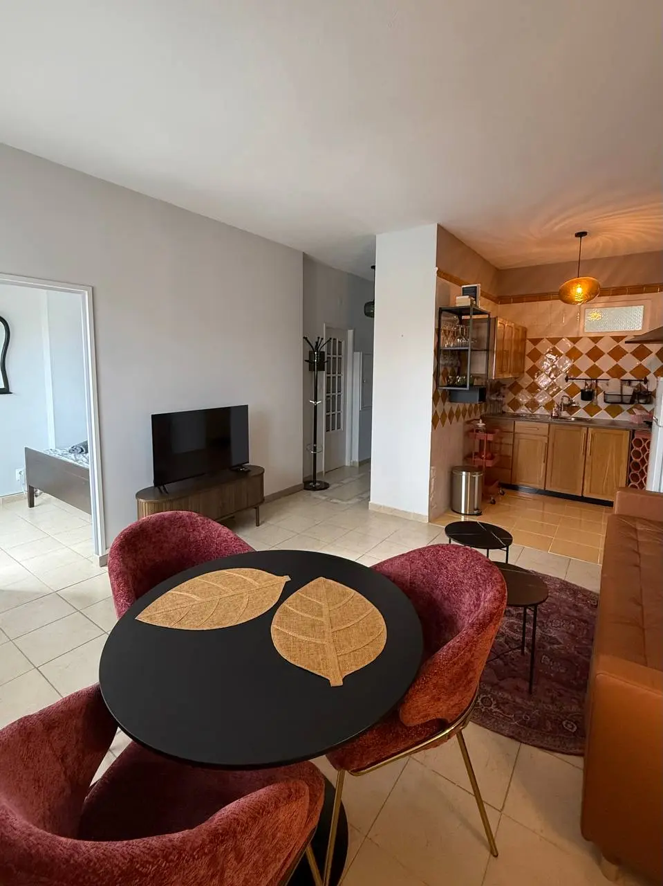 Open-plan living room with dining table, TV, sofa edge, and kitchen in the background